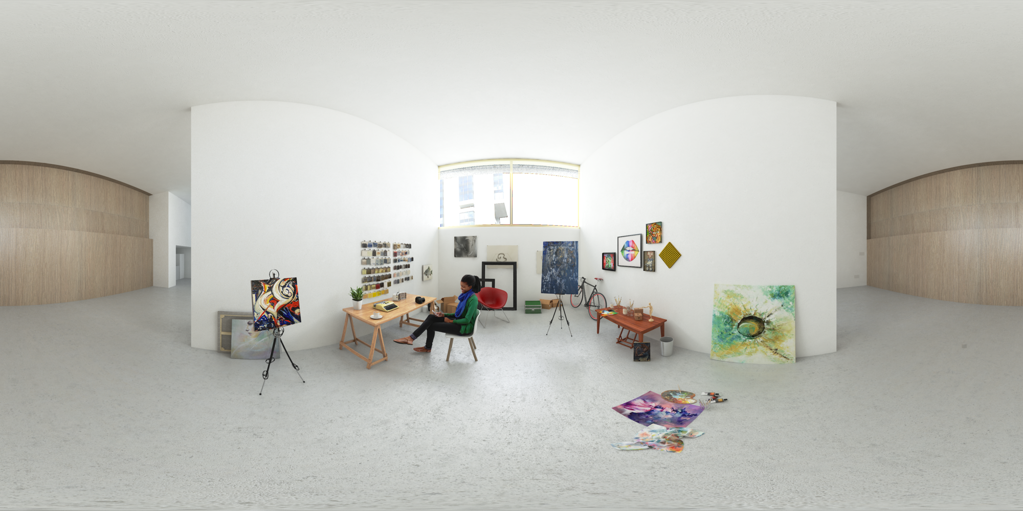 Woman sitting an a chair at a desk in a white gallery room surrounded by art pieces.