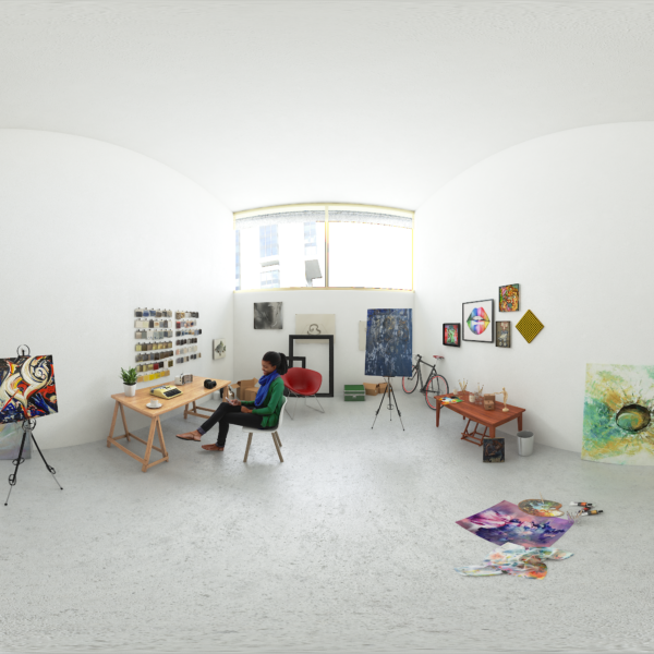 Woman sitting an a chair at a desk in a white gallery room surrounded by art pieces.