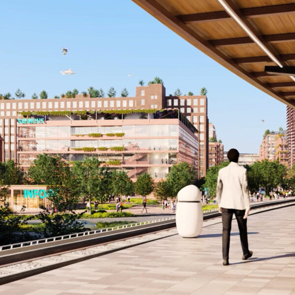 People waiting an a platform, a modern industrial area in the background.